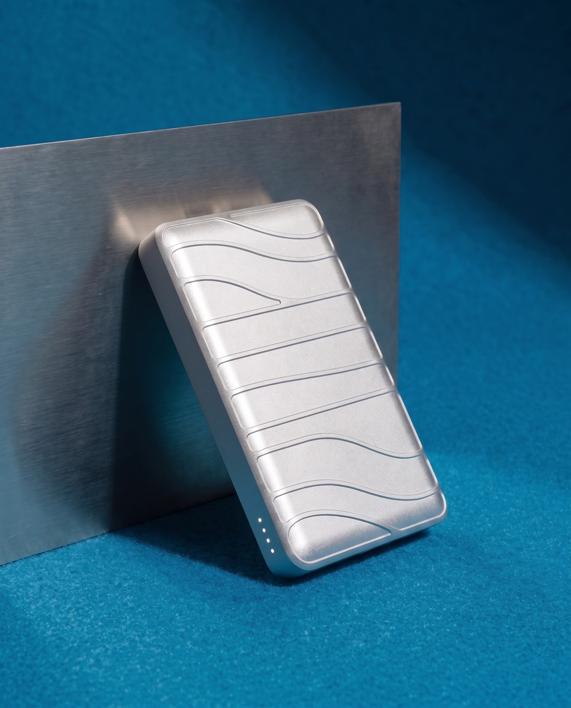 Aria power bank leaning against a brushed steel panel on azure felt